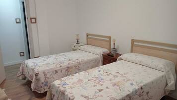 Quarto com duas camas de solteiro, cada uma com cabeceira de madeira e mesa de cabeceira com abajur.