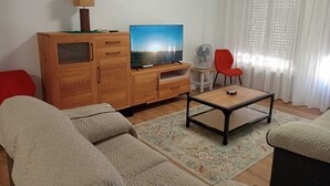 Una sala de estar con un mueble de madera, un televisor, un sillón rojo y un sofá.