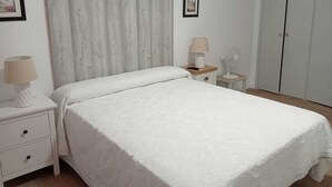 Un dormitorio con cama, mesita de noche, lámpara, ventilador y armario.
