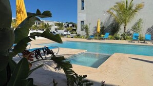 Une piscine entourée de chaises longues, de palmiers et d’un bâtiment au design moderne.