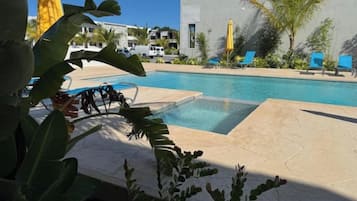 Una piscina con sillones de descanso, rodeada de palmeras y un edificio de diseño moderno.