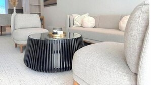 A modern living room with a round glass coffee table, two armchairs, a sofa, and a decorative vase. - New 1bd Gated Pool Beach and Gym access (Nassau)