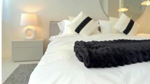 A neatly made bed with white and black pillows, a black throw blanket, and a bedside lamp on a white nightstand. - New 1bd Gated Pool Beach and Gym access (Nassau)