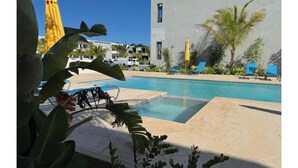 A swimming pool with lounge chairs and umbrellas, surrounded by palm trees and a modern building. - New luxury 1bd - Gated - Pool,  Beach and Gym access - Quiet and Relaxing (Nassau)