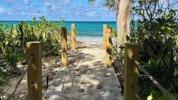 Un sentier menant à une plage, bordée d’une clôture en bois et d’une végétation tropicale.