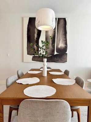 Un tavolo da pranzo con sottopiatti, un vaso bianco con una pianta e una lampada a sospensione moderna.