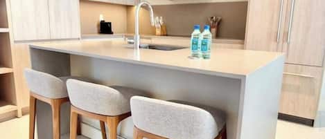 A modern kitchen with a central island, two bar stools, and a sink.