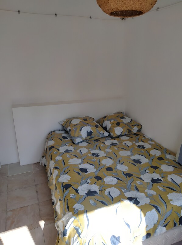 A bed with a floral bedspread, a headboard, and a hanging basket. - Urban Holiday Home with Tree-Filled Garden (Saumur)