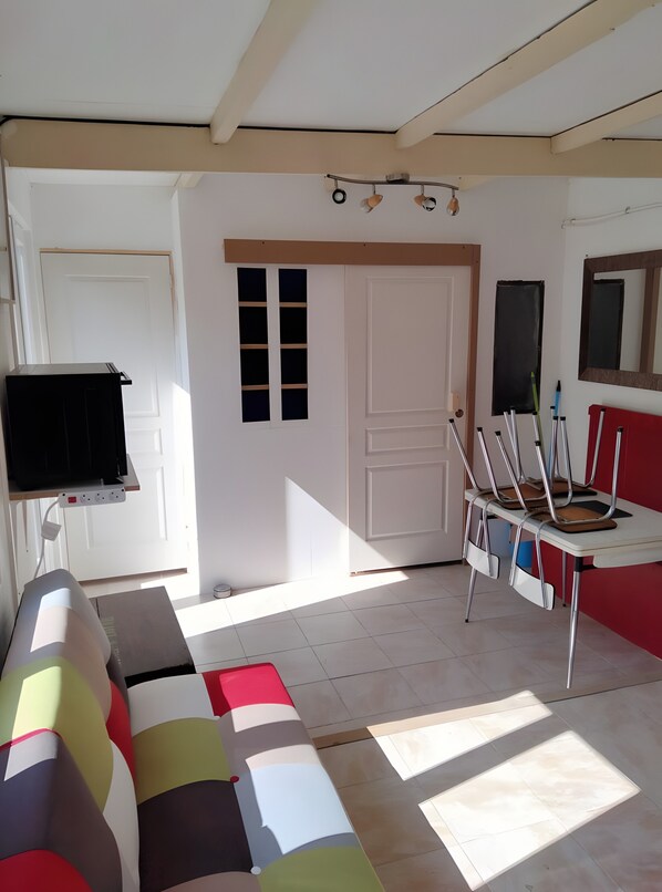 Una habitación con sofá, televisor, escritorio y sillas, y una puerta.