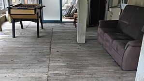 Una stanza con pavimento in legno, un divano, un tavolo da calcio e una porta che dà sull'esterno.