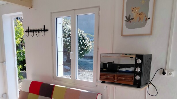A room with a colorful sofa, a wooden chest, a radio, and a window with a view of greenery. - House with Tree-filled Garden (Saumur)