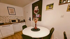 Een eethoek met een witte tafel, groene stoelen, een vaas met gedroogde bloemen en een poster aan de muur.