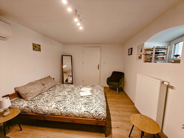 A bedroom with a bed, a chair, a desk, a mirror, and a radiator.
