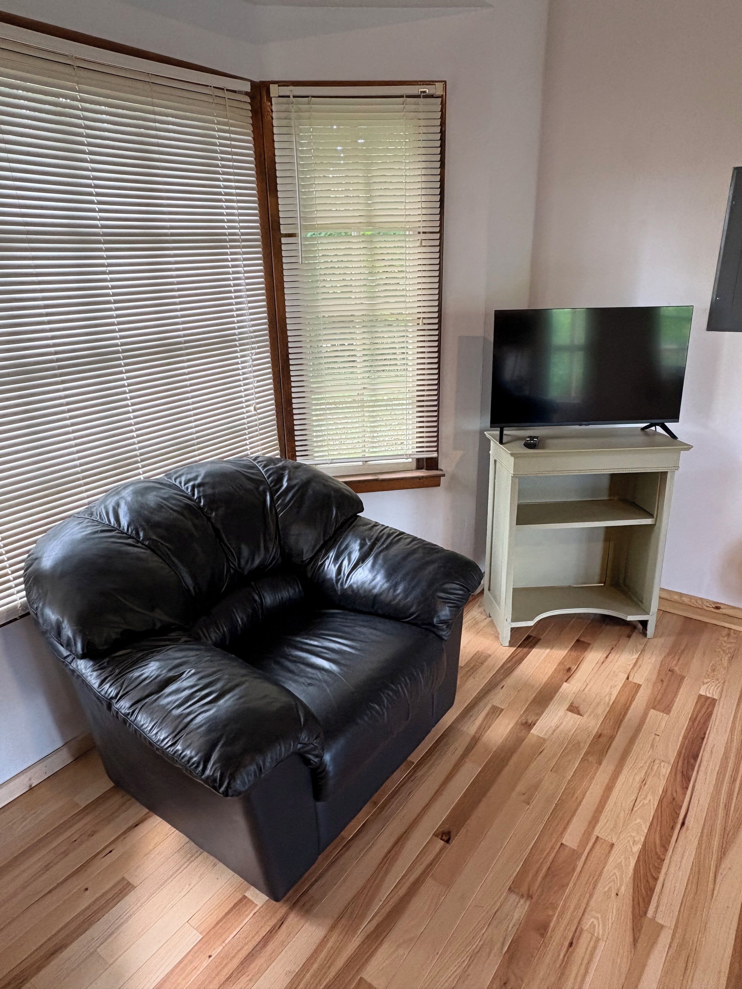 A living room with a black leather sofa, a television on a stand, and wooden flooring.