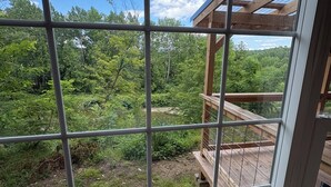 A view through a window with a grid pattern, overlooking a wooden deck and lush greenery.