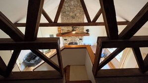 A view from a wooden-framed attic room with a stone wall and a fan.