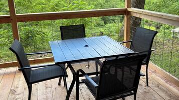 A covered wooden deck with a table and chairs, overlooking a forested area.