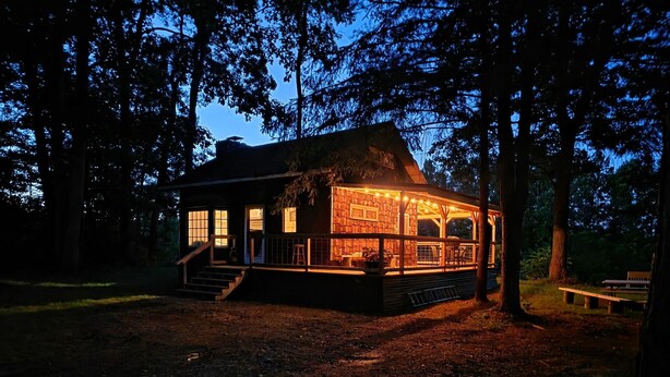 A rustic cabin with a thatched roof, wooden exterior, and a porch with string lights.