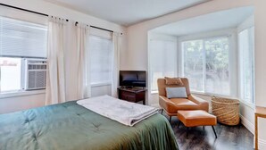 Una habitación de hotel con cama, televisión, sillón de cuero y ventana con persianas.