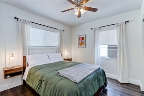 A bedroom with a bed, bedside lamps, a ceiling fan, and a window with curtains.
