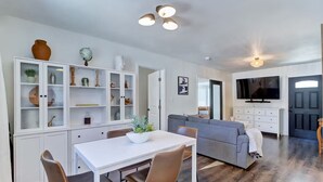 Una sala moderna con un sofá gris, una mesa de comedor con sillas y un mueble blanco con puertas de cristal.