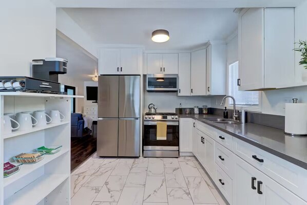A modern kitchen with white cabinets, stainless steel appliances, and a marble floor.