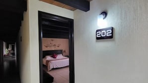 A hallway leading to a bedroom with a bed, a nightstand, and a wall-mounted light fixture. - Hotel Villalba (Comitán de Dominguez)
