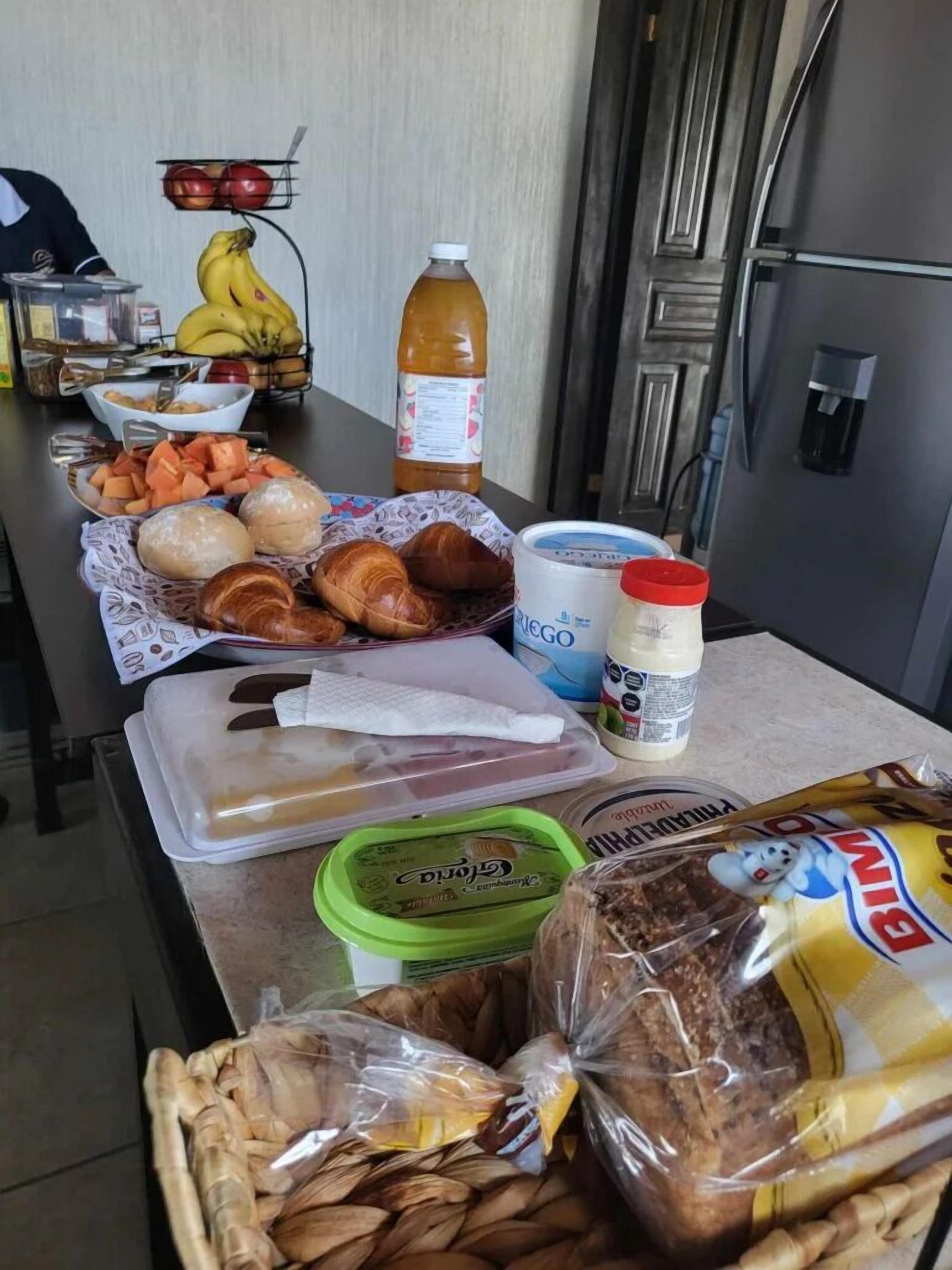 Una encimera de cocina con diversos alimentos y condimentos, como pan, queso y una botella de jugo.