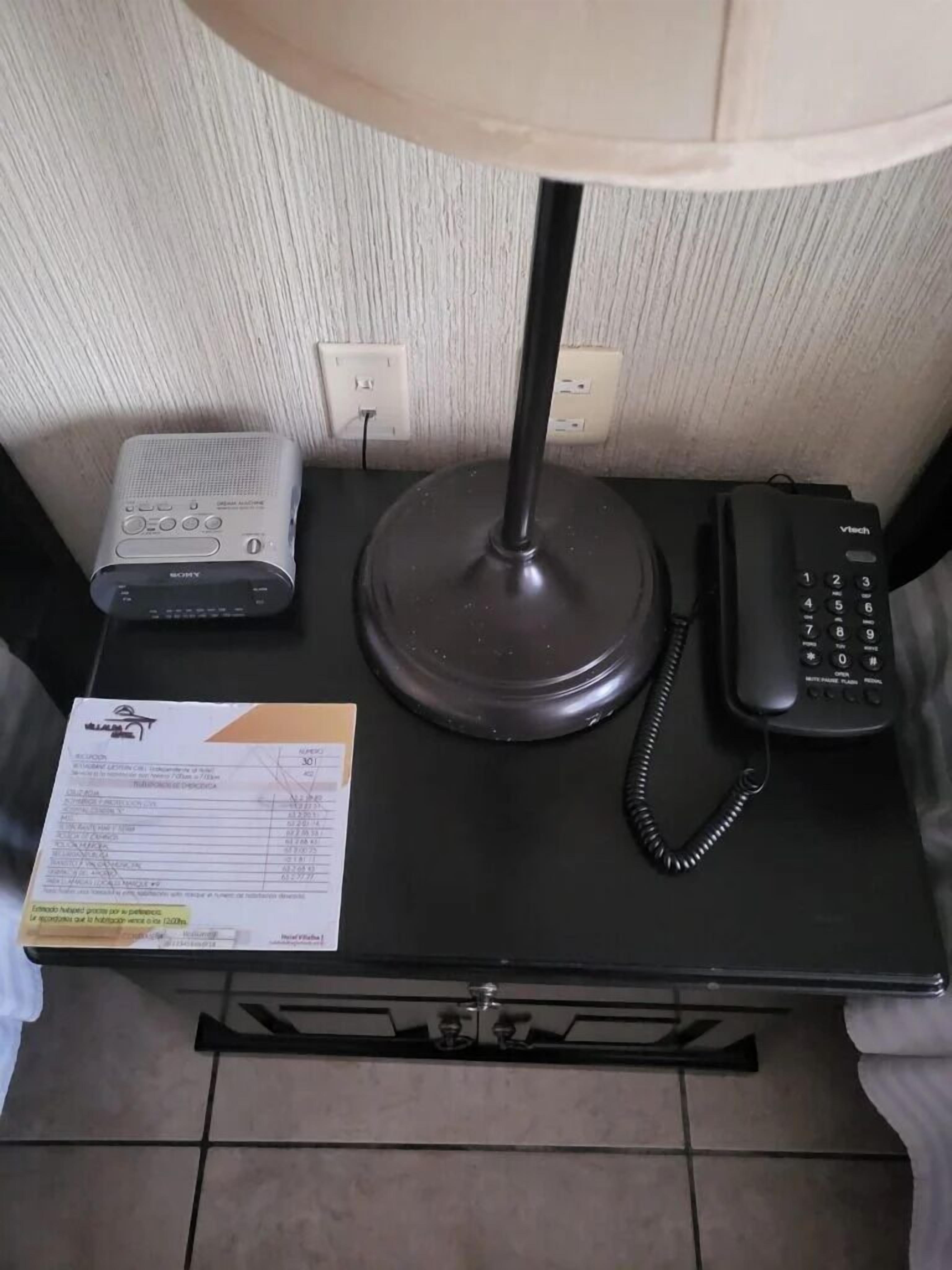 Un escritorio con una lámpara, un sistema de audio Sony, un teléfono y un recibo.