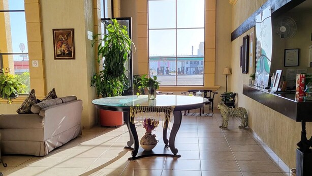 A spacious lobby with a large arched window, a reception desk, a round table, and several potted plants. - Hotel Villalba (Comitán de Dominguez)