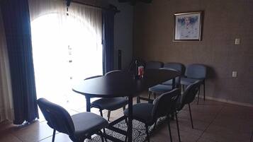 A dining area with a round table and six chairs, a framed picture on the wall, and a window with curtains.