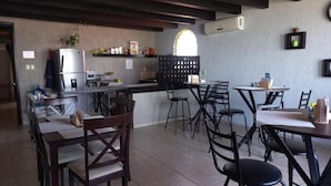 A restaurant with wooden furniture, a kitchen area, and a large window. - Hotel Villalba (Comitán de Dominguez)