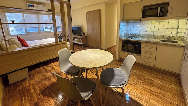 A compact living space with a round dining table, two chairs, a kitchenette, and a window with a view. - Rent Up - Monoambiente Zona Congreso (Buenos Aires)