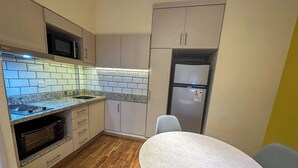 A compact kitchen with a microwave, oven, and refrigerator. There is a dining table with two chairs. - Rent Up - Monoambiente Zona Congreso (Buenos Aires)