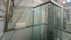 A glass-enclosed shower with a marble wall and a tiled border. - Rent Up - Monoambiente Zona Congreso (Buenos Aires)
