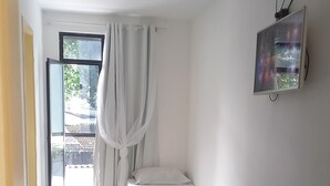 Ein Zimmer mit Bett, Deckenventilator, Fernseher und einem Fenster mit Vorhängen.