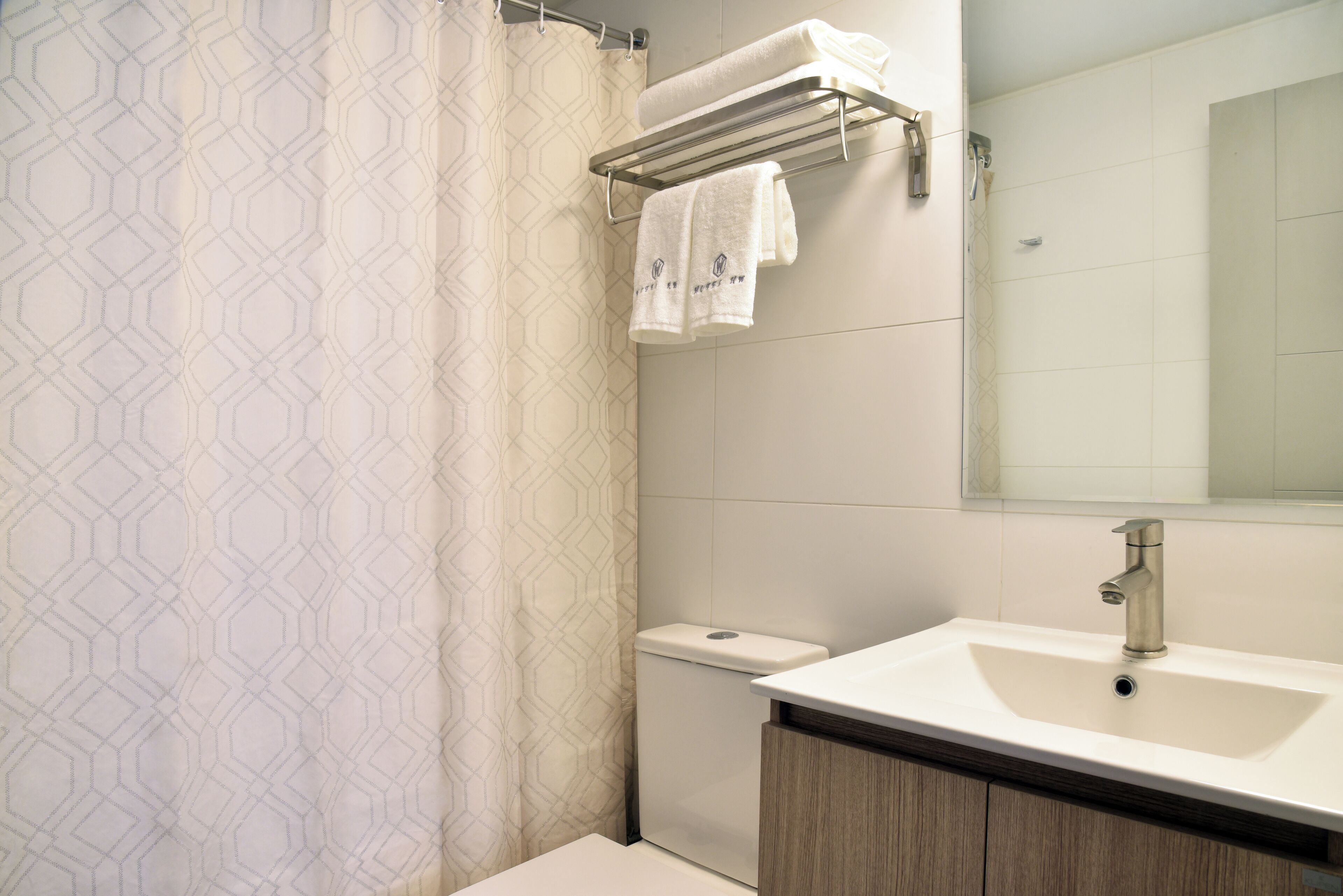 A modern bathroom with a shower curtain, a toilet, a sink with a mirror, and towels on a rack.