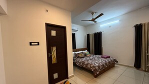 A bedroom with a bed, a ceiling fan, a window with curtains, and a door with a doormat.