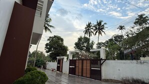 A residential street with a gated entrance, a modern building, and palm trees.