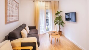 A living room with a dark grey sofa, a small wooden table, a potted plant, and a mounted TV.