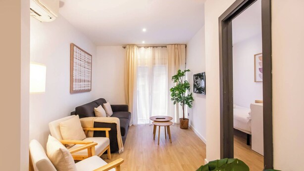 A living room with a sofa, chairs, a small table, and a potted plant.