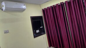 Una habitación con aire acondicionado de pared, un ventanal pequeño con marco negro y una puerta con marco amarillo.