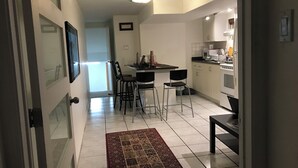 A modern kitchen with white cabinets, a dining area with bar stools, and a small table. - Beautiful Fully Furnished Two Bedrooms - Basement Apartment (Toronto)