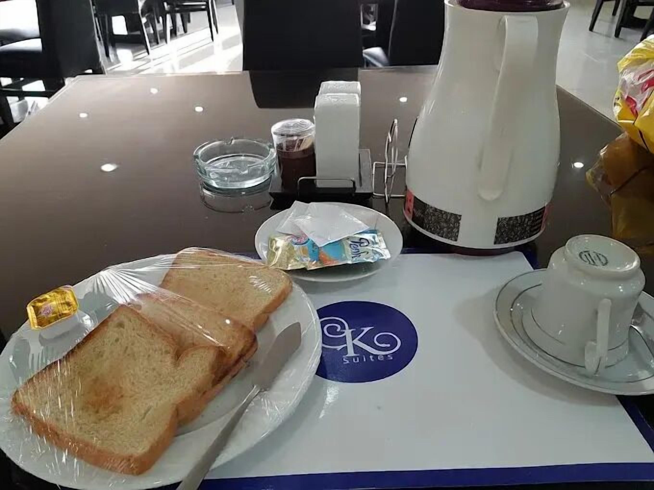 A breakfast table with a coffee pot, a cup, a plate with toast, a glass of water, and a small container of jam.