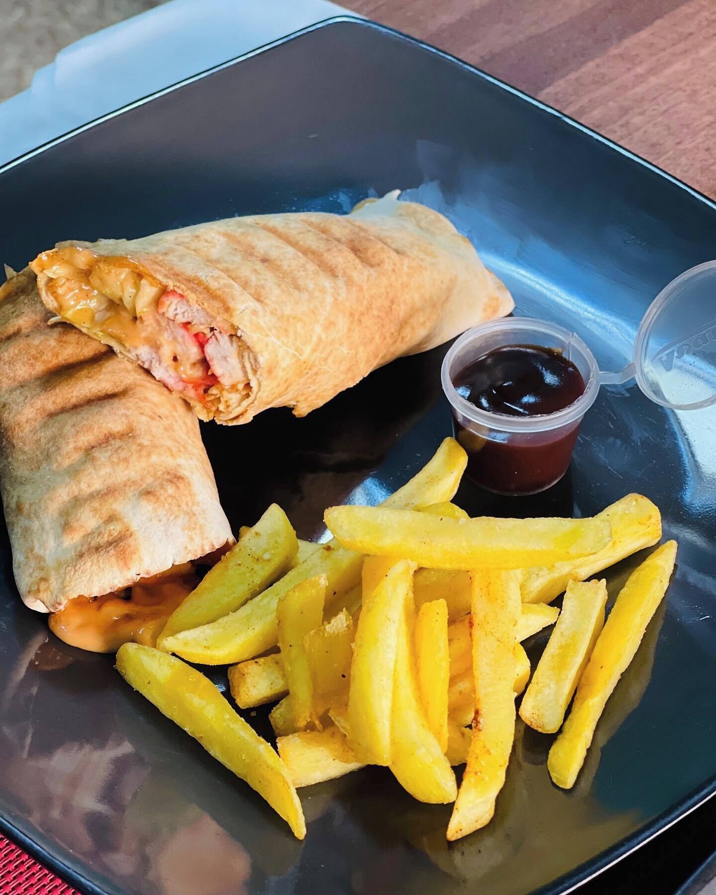 A plate with a wrap, fries, and a small container of sauce.