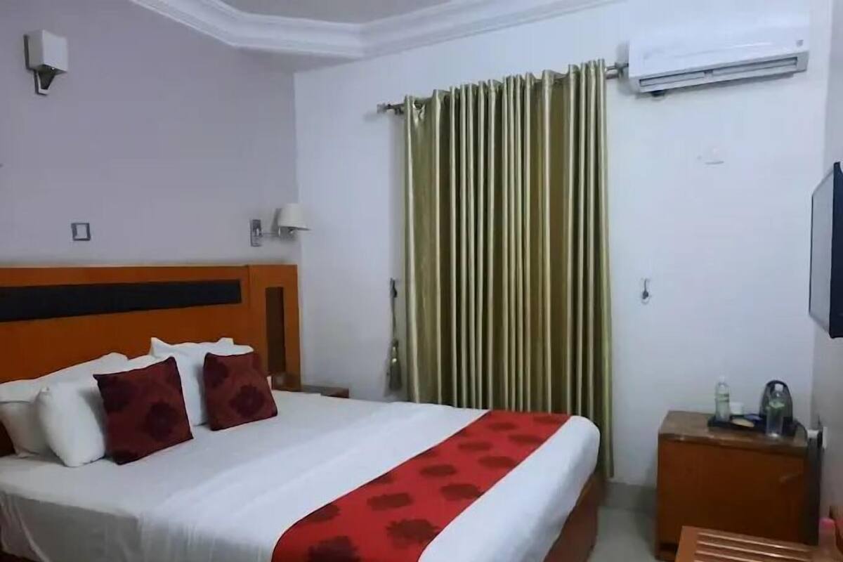 A hotel room with a bed, a nightstand, an air conditioning unit, and a curtain.