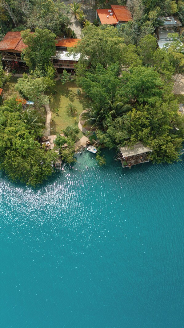 Vista aérea de una isla tropical con un mar turquesa cristalino, rodeada de exuberante vegetación y varias pequeñas construcciones con tejados rojos.