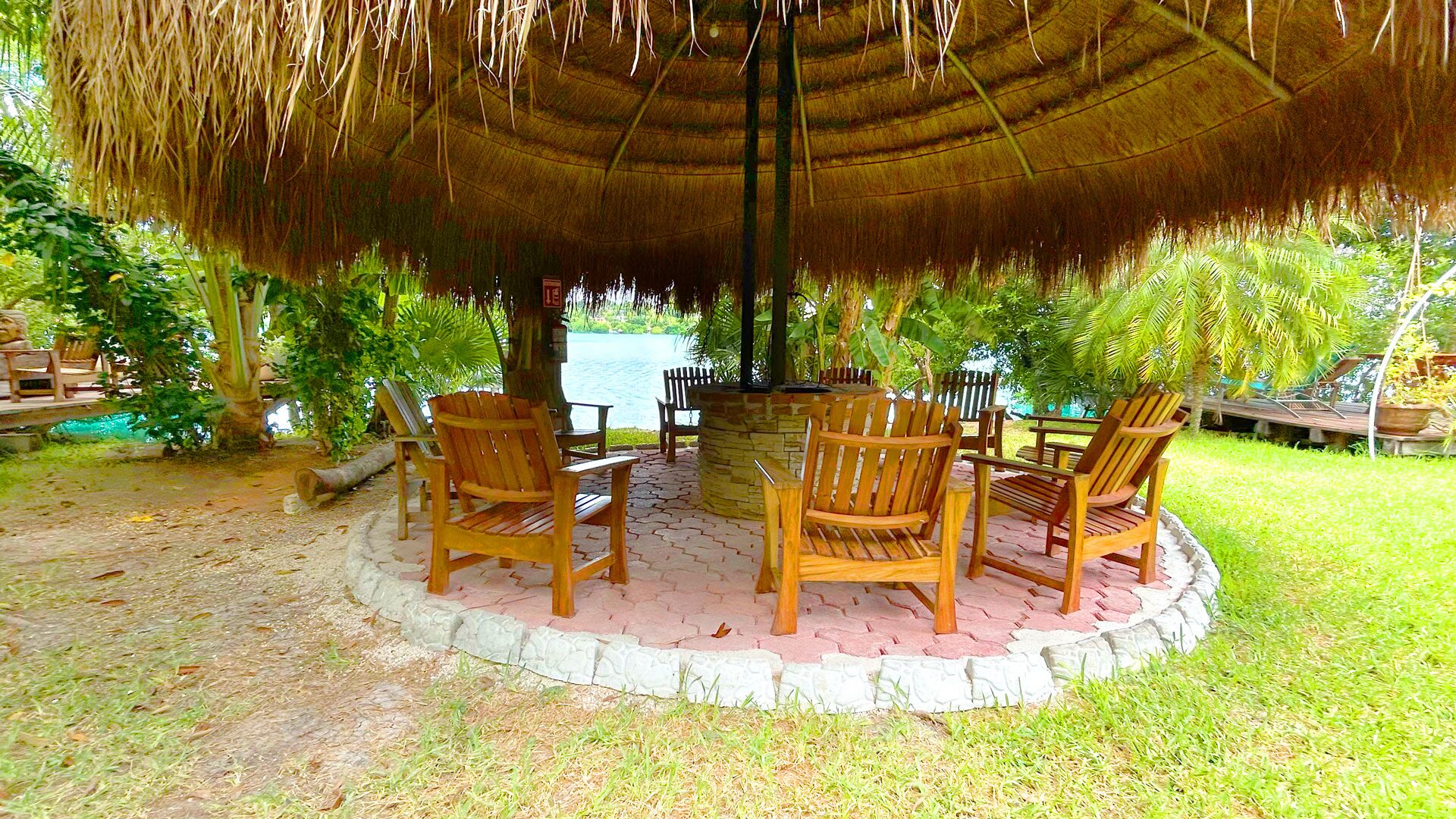 A thatched gazebo with wooden chairs and a table, surrounded by lush greenery.