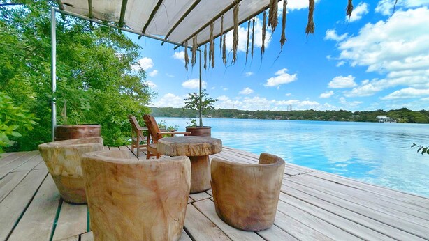 A wooden deck with outdoor seating and a view of a lake. - Hotel Xu-La Azul (Xul-Ha)