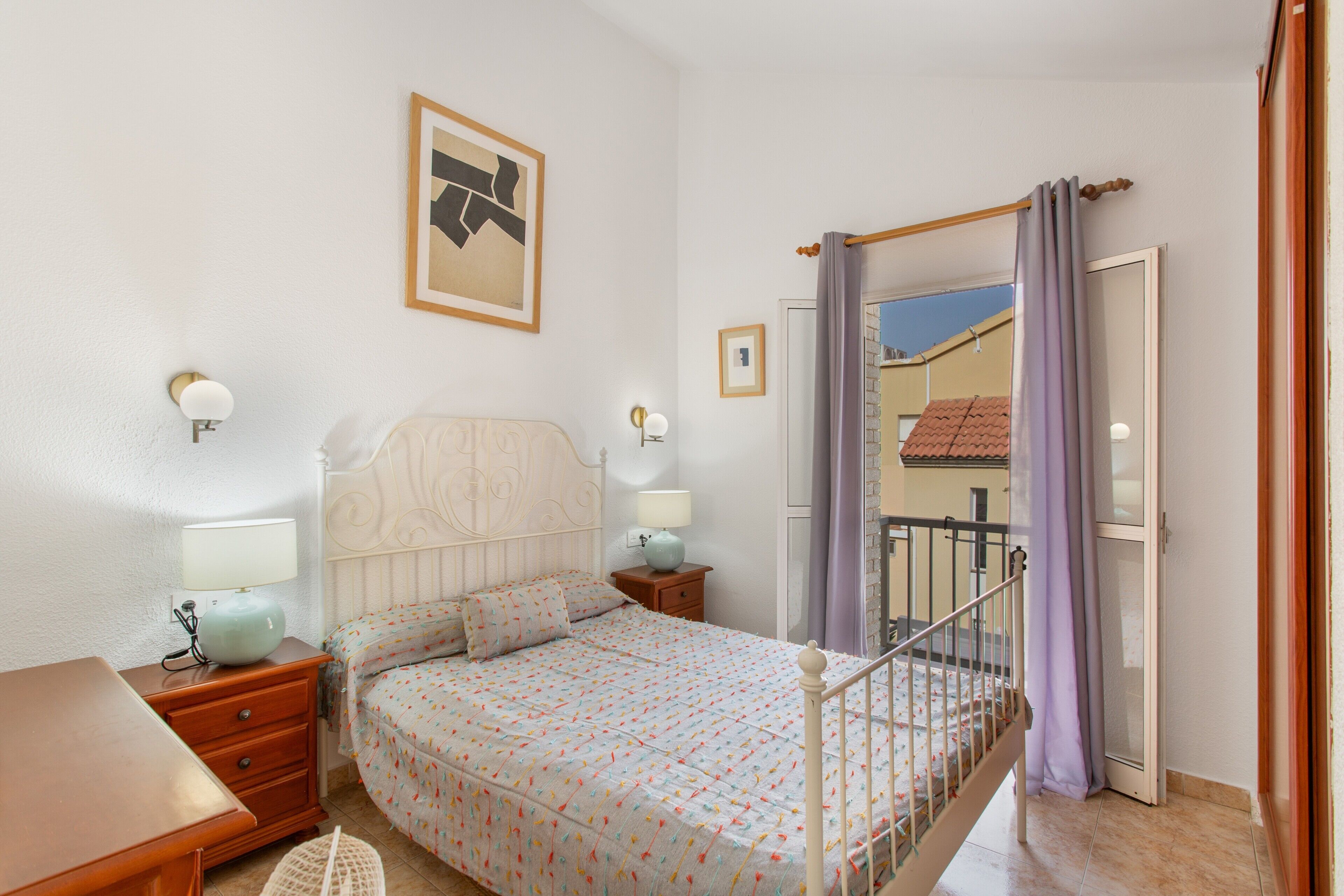 Un dormitorio con cama, mesitas de noche, cortinas y vistas al exterior.